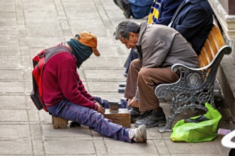 A shoeshine boy works on a pavement polishing the shoes of a seated man, shoeshine boy in the