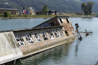 Partially submerged ship with graffiti near shore with mountains, at the harbour Linz Upper Austria