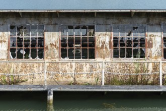Abandoned building with broken windows and rust next to a body of water, at the harbour of Linz