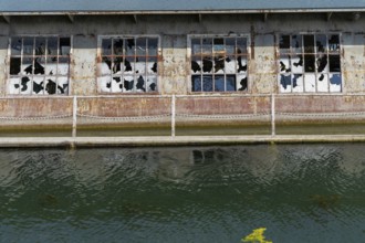 Dilapidated building with broken windows and rusty structures on the waterfront, at Linz harbour