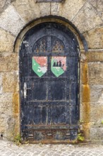 Old door with coat of arms on a stone wall, surrounded by rust and weathering, Pöstlingsbergkirche