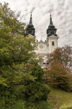 Historic church with two towers behind autumnal trees in front of a cloudy sky, Pöstlingsbergkirche