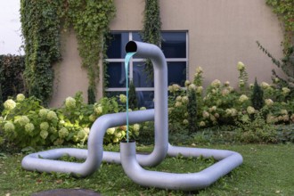 Metal sculpture in the garden with flowing coloured water and plants in the background, city centre