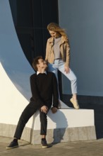 Two young adults share a light-hearted moment by a large curved structure in an urban setting. The