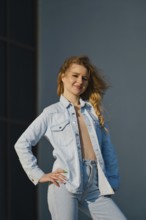 A young woman stands confidently, showcasing a light denim jacket and high-waisted jeans. The