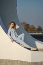 A woman with long hair is sitting comfortably on a curved architectural element. She wears a light