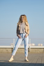 A woman stands on a rooftop during a bright sunny day. She is wearing a light fleece jacket and