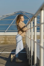 A young woman stands by the observation deck, leaning on a white railing. She gazes out at the
