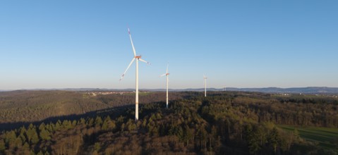A row of wind turbines towers over a wooded hill under a clear sky, near Schorndorf in the Rems