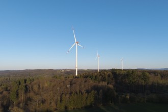 Three wind turbines stand in a wooded landscape under a clear sky, near Schorndorf in the Rems