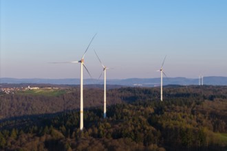 Several wind turbines stretch across a wooded landscape under a clear sky, near Schorndorf in the