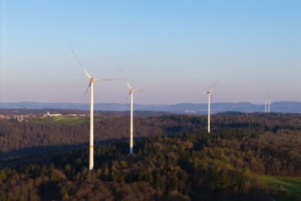 Wind turbines standing on a hill above a forest, seen against a calm sky, near Schorndorf im