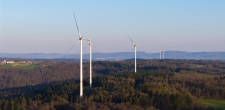 Wind turbines stand on a forest landscape with a clear blue sky in the background, near Schorndorf