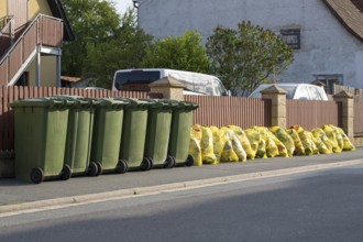 Green bins for organic waste and yellow bags for plastic waste at the roadside, waste separation,