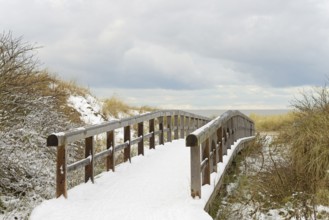 Winter day, onset of winter, wooden plank path leads through the snow-covered dune landscape to the
