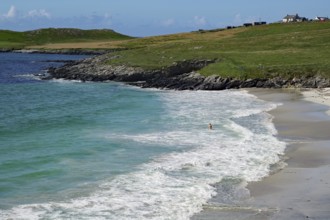 Coastline with white sand and gentle waves on a clear blue day, solitary figure in the water,