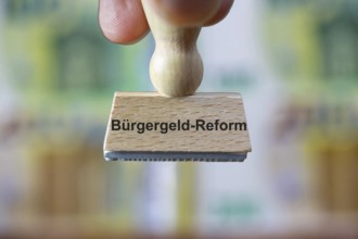 (Photomontage) Stamp with the inscription BÜRGERGELD in front of blurred euro banknotes in the