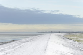 North Sea coast on a winter's day, people walking over a snow-covered dyke, the island of Norderney
