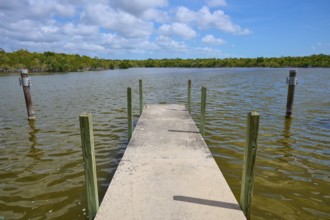 A concrete footbridge leads into the water, surrounded by tranquil nature and cloudy skies, West