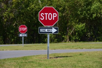 Stop signs and one-way street signs in front of a green tree landscape, Flamingo, Everglades