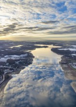 Aerial view of Lake Möhnesee in winter with snow and reflections of clouds on the water surface at