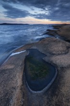 Rocks on the coast with puddle of water while evening light shines through clouds on the horizon,