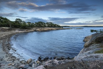 Small bay with sandy beach, surrounded by rocks and pine trees under a partly cloudy sky, Skjeberg,