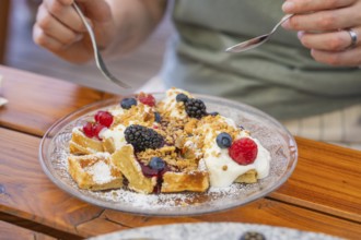 Person enjoying waffles with cream and berries on a wooden table