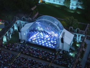 Night shot of an illuminated open-air stage in front of an audience in ruins