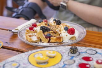 Waffles with cream and berries on a plate, close-up on a wooden table