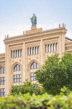 Large historic building with statue on the roof, surrounded by green vegetation, Munich, Germany