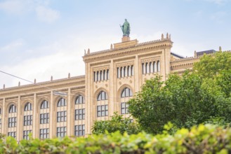 View of a historic building with a statue on the roof, surrounded by green foliage, Munich, Germany