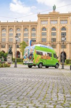 A colourfully painted bus in front of a historic building with a cobbled street and lanterns,