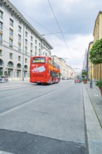 A red double-decker bus on an empty street in Munich under a cloudy sky, Munich, Germany