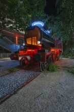 Luminous steam engine as an art installation surrounded by trees at night, Munich, Germany