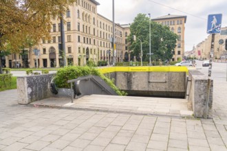 Entrance to underground station with green vegetation, surrounded by urban architecture, Munich,