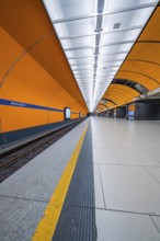Orange-coloured symmetrical underground station with modern lighting and clear lines, Munich,