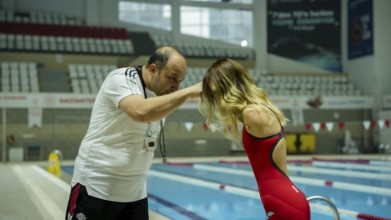A female Paralympic swimmer with amputated arms performs warm-up exercises on a mat before entering