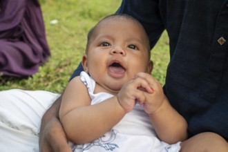Baby sits with an open mouth, appearing curious outdoors-Dhaka, Bangladesh