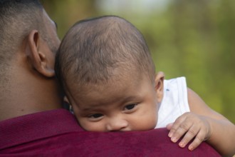 Baby rests peacefully on a man's shoulder outdoors-Dhaka, Bangladesh