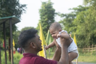 A father holds his baby, engaging in eye contact in a sunny outdoor setting-Dhaka, Bangladesh
