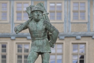 Wood carrier by Bernhard Frydag, 1914, male figure carrying basket with wood on his back, symbol