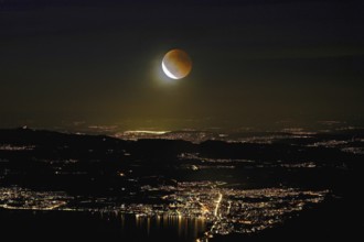 Blood moon, total lunar eclipse over the illuminated city and Lake Zug, Zug, Canton Zug,