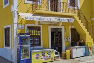 Yellow building with mini market and advertising signs, surrounded by summer flair, Kattavia