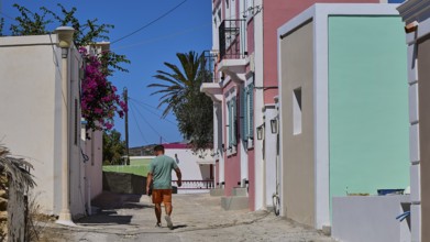 A man walks along a sunny street, past colourfully painted buildings with Mediterranean flair,