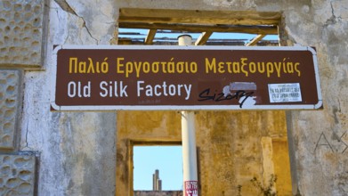 Sign of an old silk factory in Greek and English, surrounded by weathered structures, Old silk