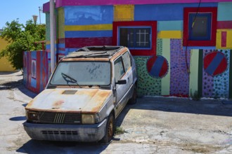 Neglected old car in front of a colourfully painted urban building, Kattavia village, southern tip