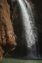 A Moroccan young man climbs the rock before jump from into the water under a waterfall Ouzoud