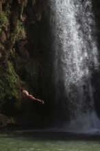 A Moroccan young man jumps from the high rock into the water under a waterfall Ouzoud