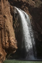 A Moroccan young man climbs the rock before jump from into the water under a waterfall Ouzoud